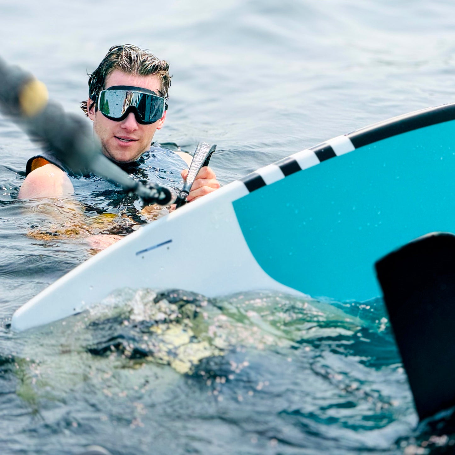 Person on a stand-up paddleboard wearing AERA Black Mirror swimming goggles for sun protection and clear vision on the water.