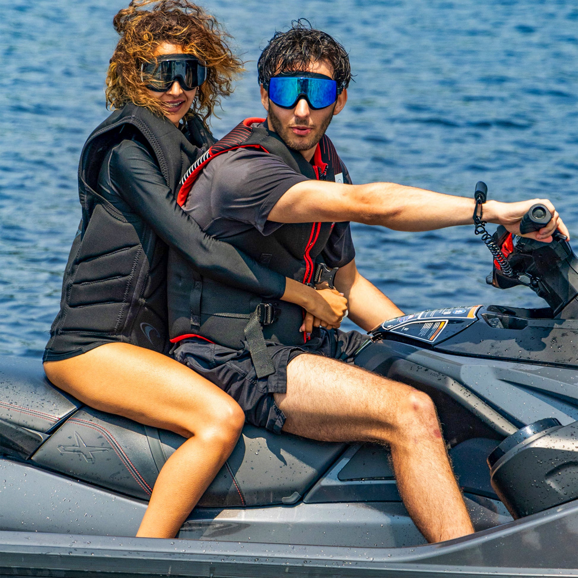 Two people riding a jet ski on the water, wearing AERA swimming goggles and life vests for sun protection and clear vision