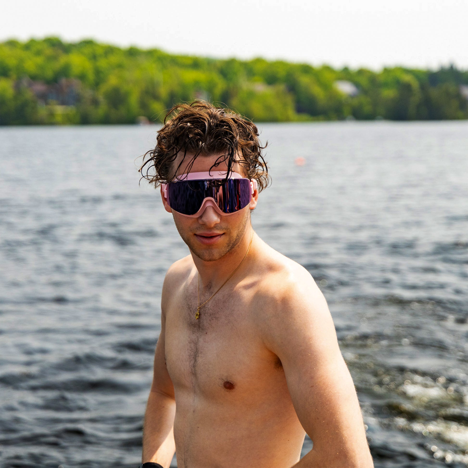 “Man wearing ÆRA Blushwave polarized swimming goggles with a lake and trees in the background, featuring anti-fog lenses and UV protection for adults