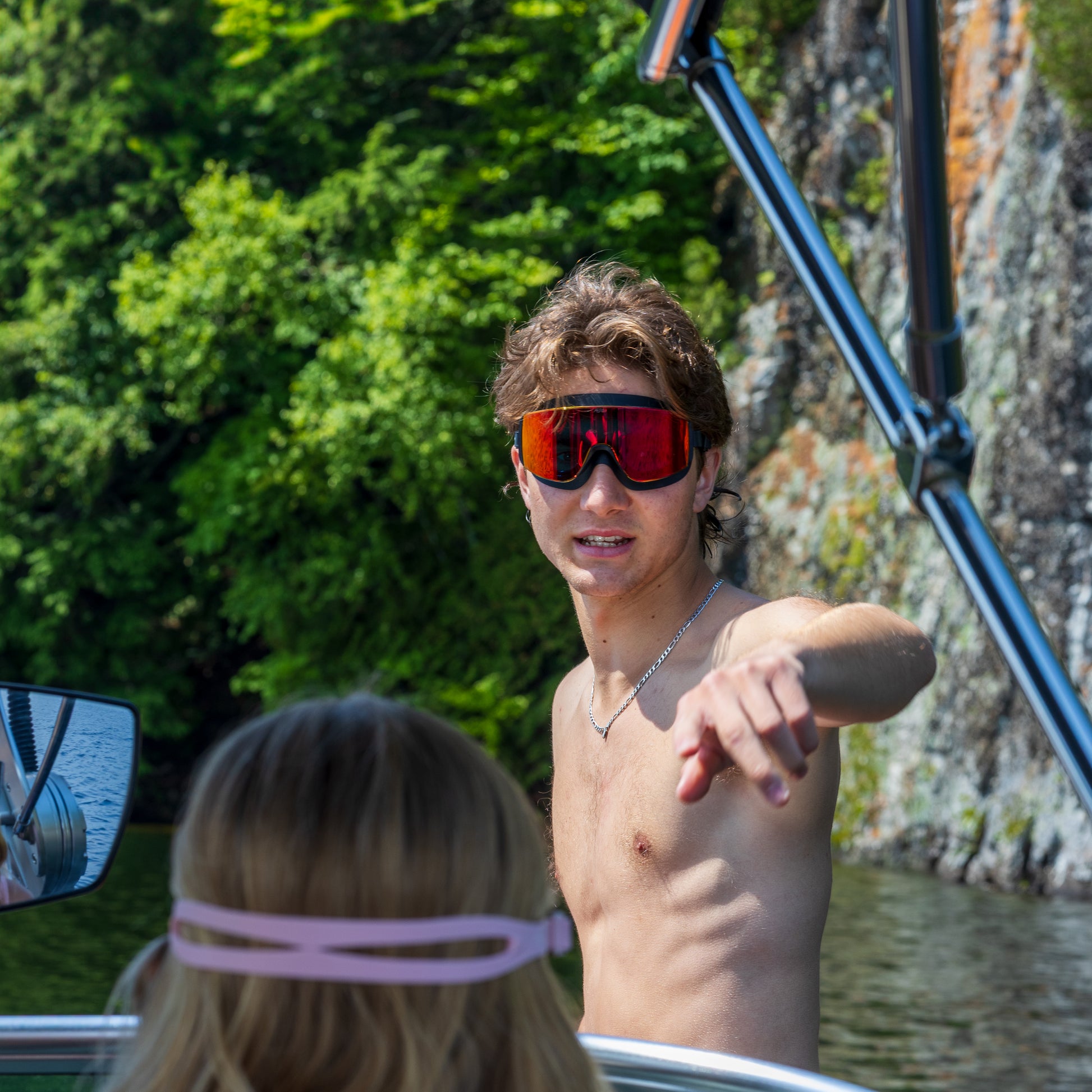 Man wearing ÆRA Fire swimming goggles and a woman wearing ÆRA Blushwave swimming goggles on a boat with a natural water and tree background, featuring anti-fog lenses and UV protection for adults
