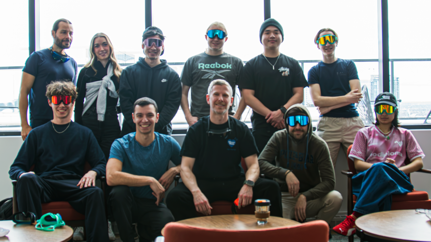 Group of people wearing colorful sunglasses/swimming goggles in an office setting.