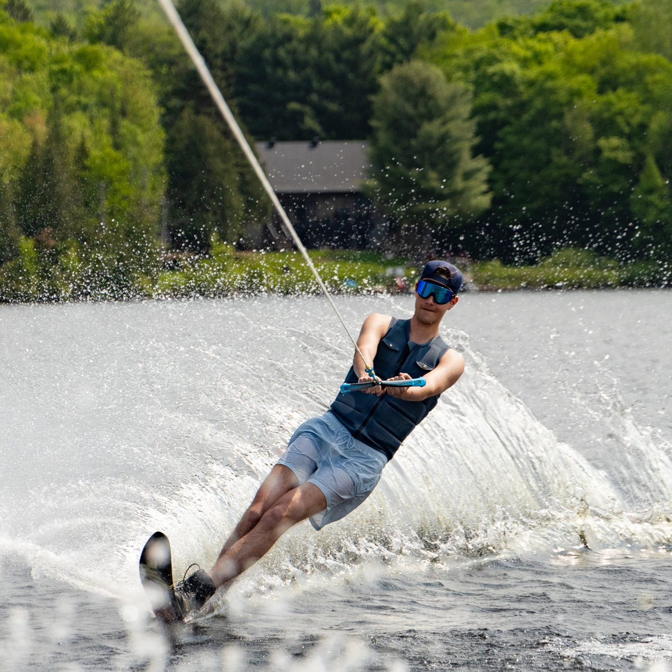 Person water skiing on a lake with trees in the background, wearing ÆRA swimming goggles with anti-fog lenses and UV protection for adults