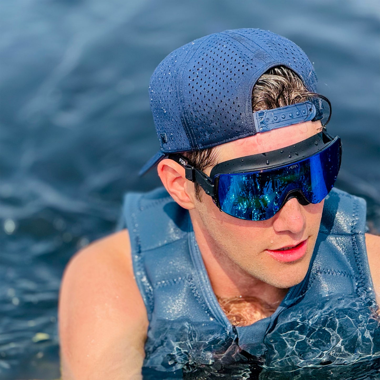 Person wearing a blue cap and reflective goggles with water in the background