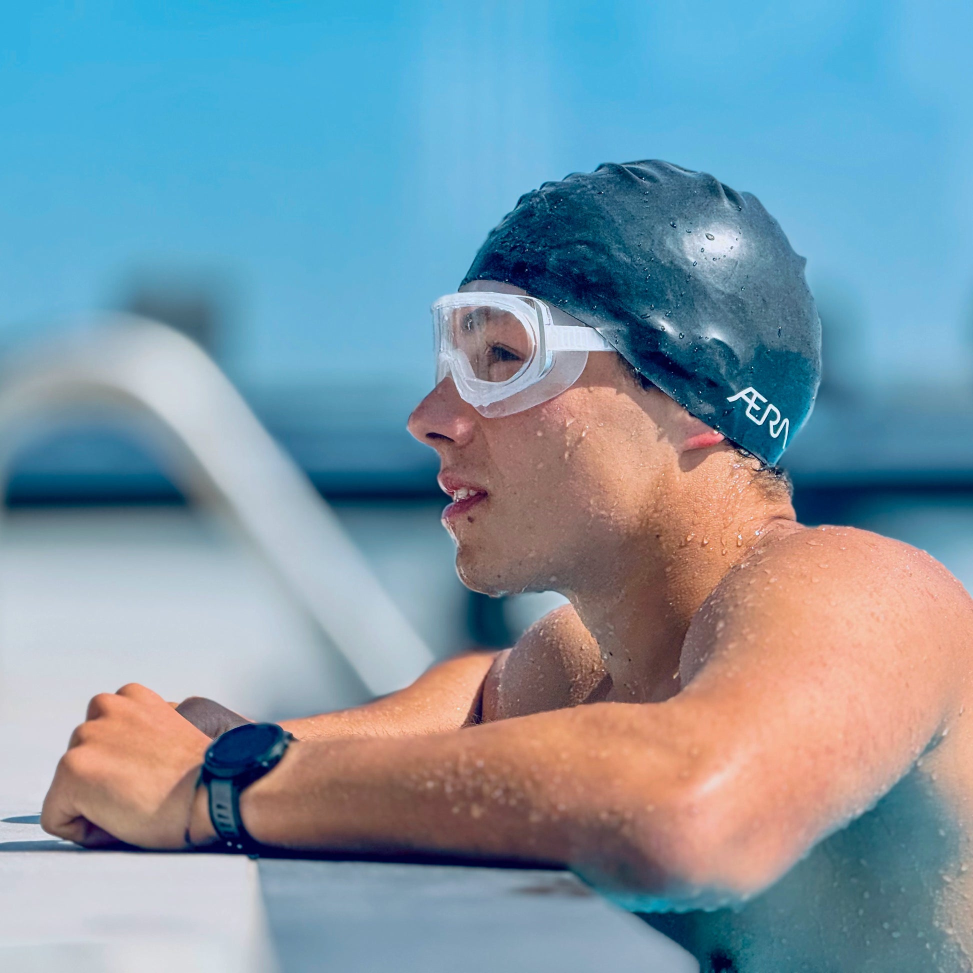 Swimmer wearing a swim cap and clear goggles, looking out of a pool.
