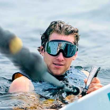 Person on a stand-up paddleboard wearing AERA Black Mirror swimming goggles for sun protection and clear vision on the water.