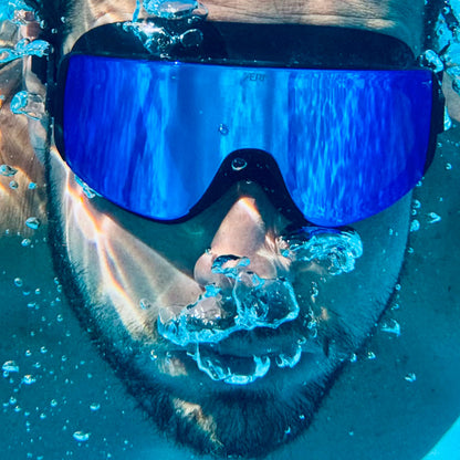 Person wearing blue goggles with water droplets on a clear blue background