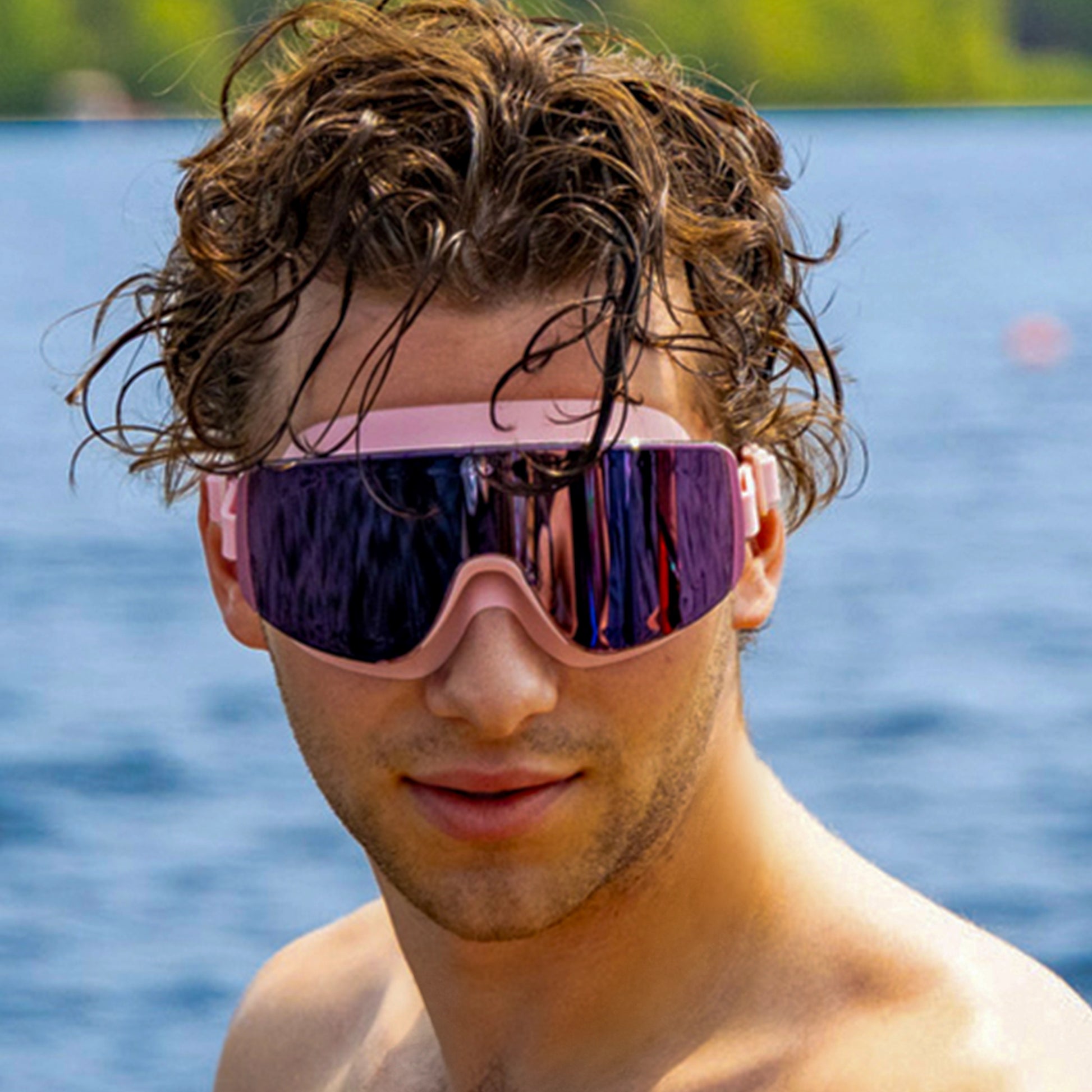 “Man wearing ÆRA Blushwave polarized swimming goggles with a lake and trees in the background, featuring anti-fog lenses and UV protection for adults