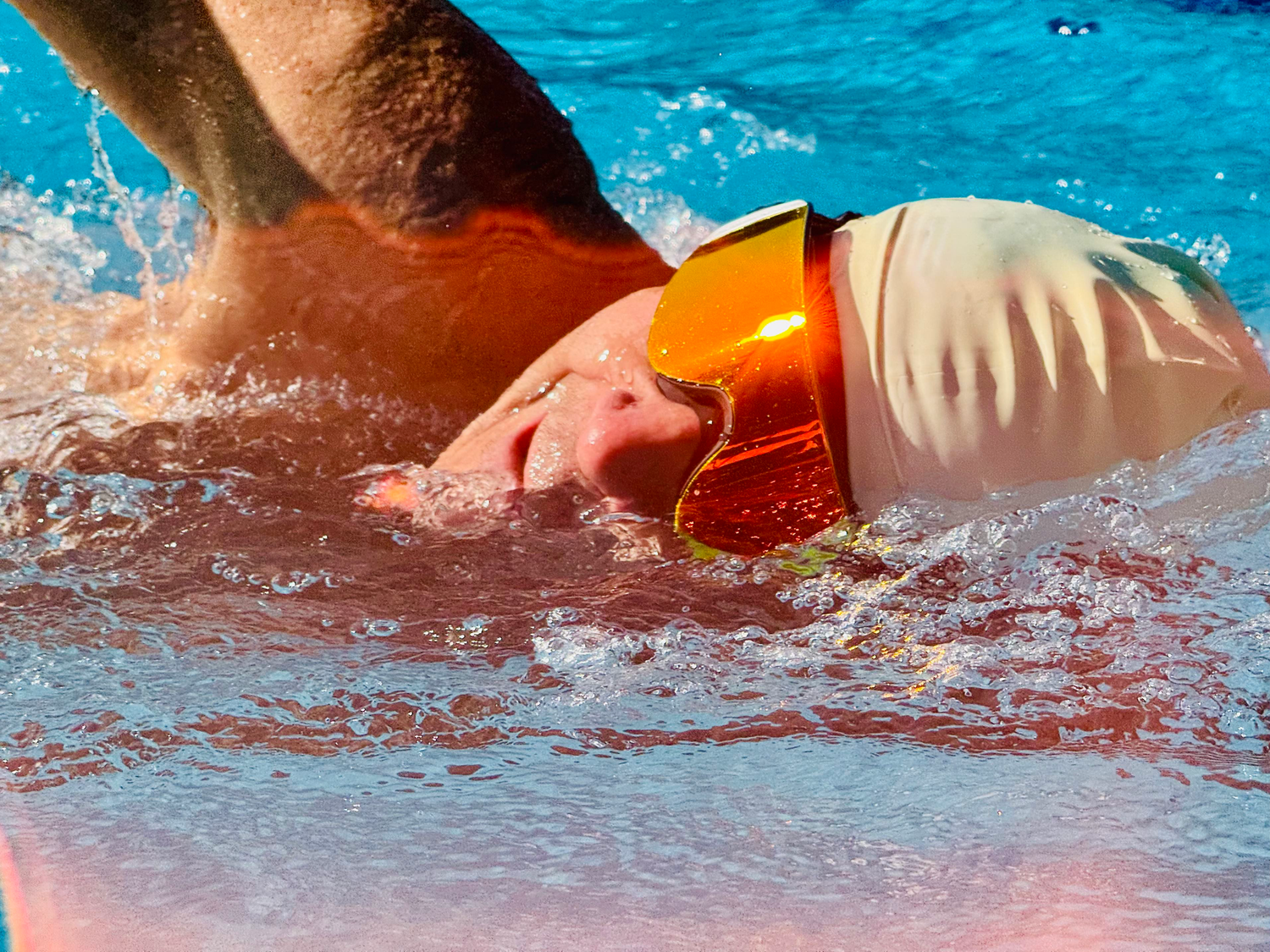 Male swimmer wearing AERA Sports goggles in bright sunlight with lens reflecting sun, showcasing UV protection